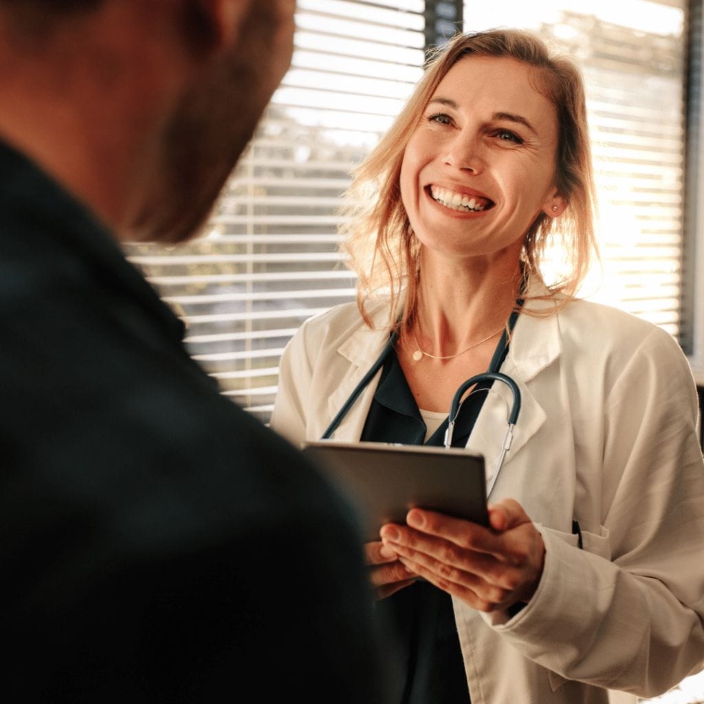 Blonde Doctor Holding a Clipboard Smiling at Patient Inside Doctors Office
