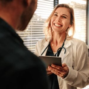 Blonde Doctor Holding a Clipboard Smiling at Patient Inside Doctors Office