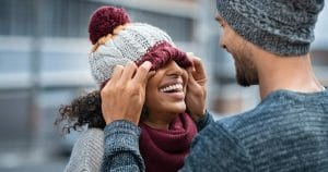 male and female wearing jackets and hats for cold weather. Man putting hat over woman's eyes and smiling